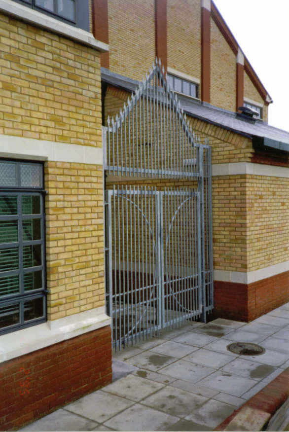 Metal gate in brick building entrance; light brown brick, gray sidewalk, spiky top.