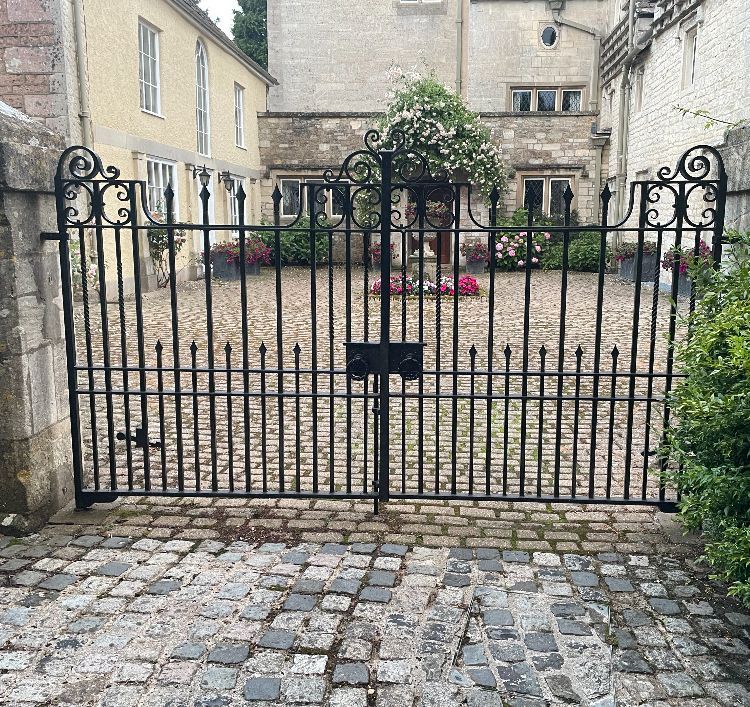 Black wrought-iron gates in front of a cobblestone courtyard. A flowering plant is in the center.