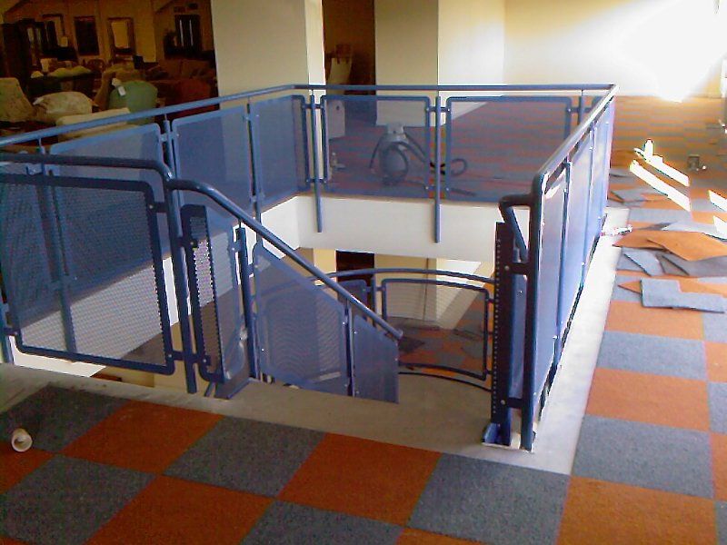 Blue metal railing surrounds a staircase in a building, with checkered orange and gray floor.