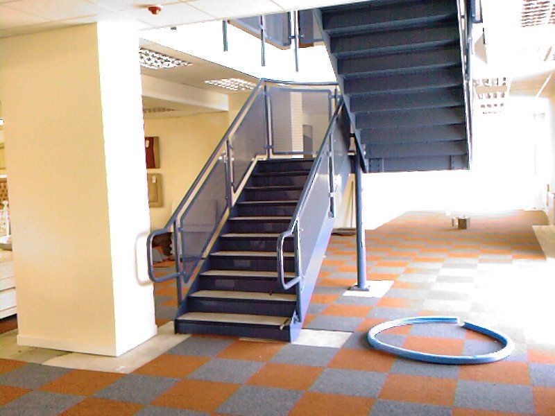 Staircase with blue metal railings and steps, leading upward. Brown and gray checkerboard floor.