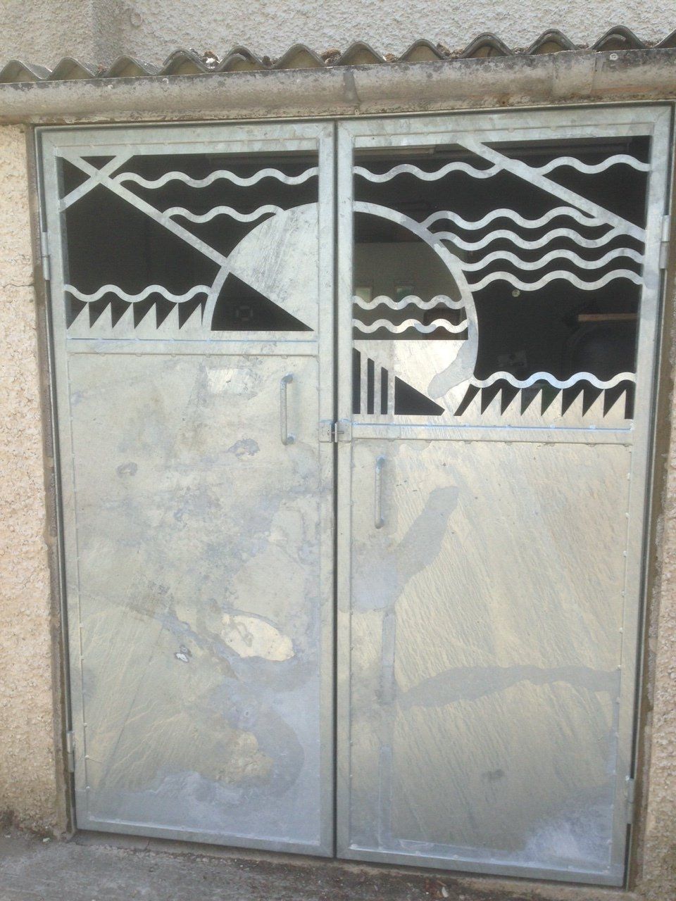 Two metal doors with decorative cutouts featuring a sun, waves, and geometric shapes.