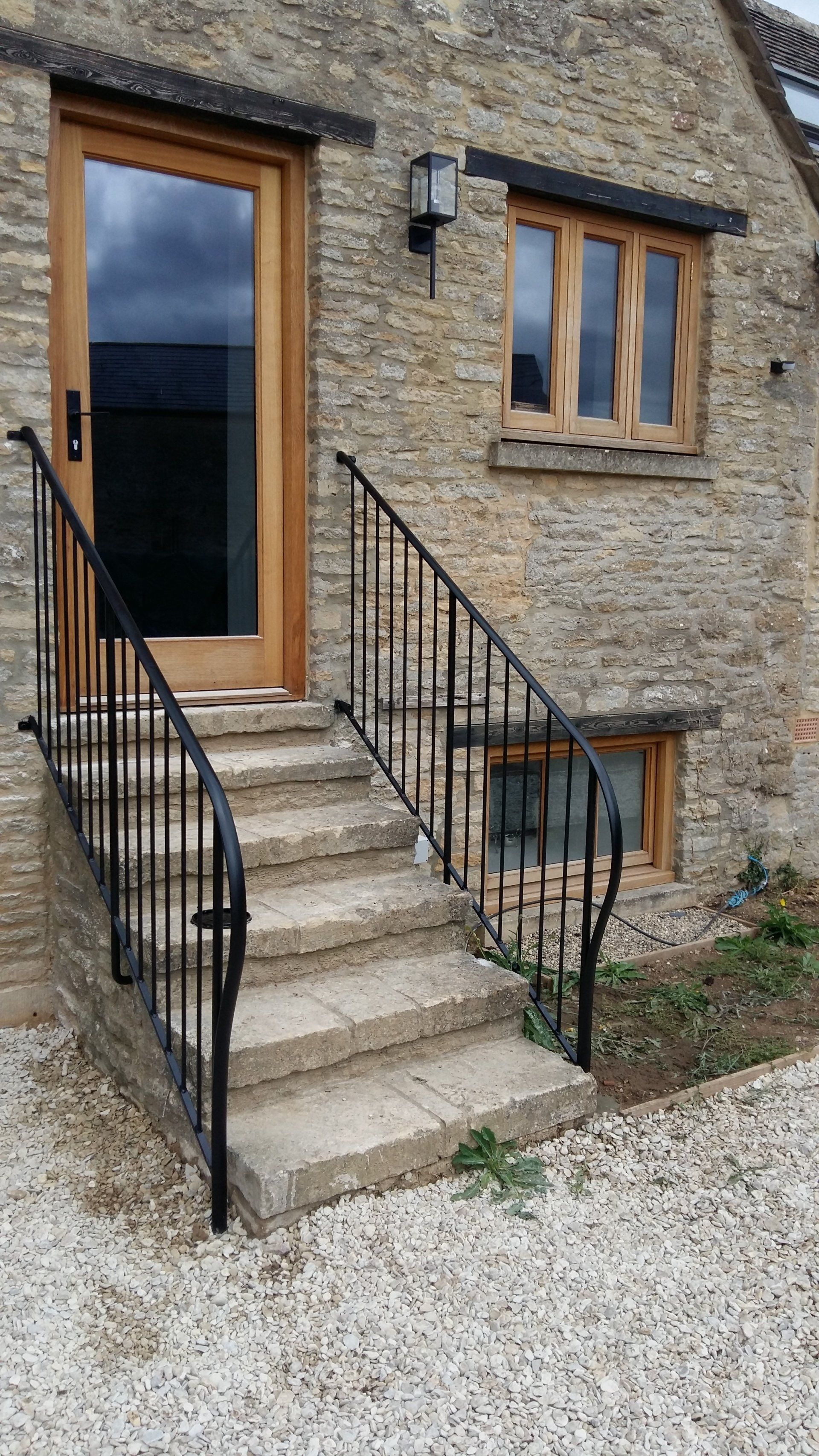 Stone steps leading to a wooden door and window, with black metal handrails. Beige stone building.