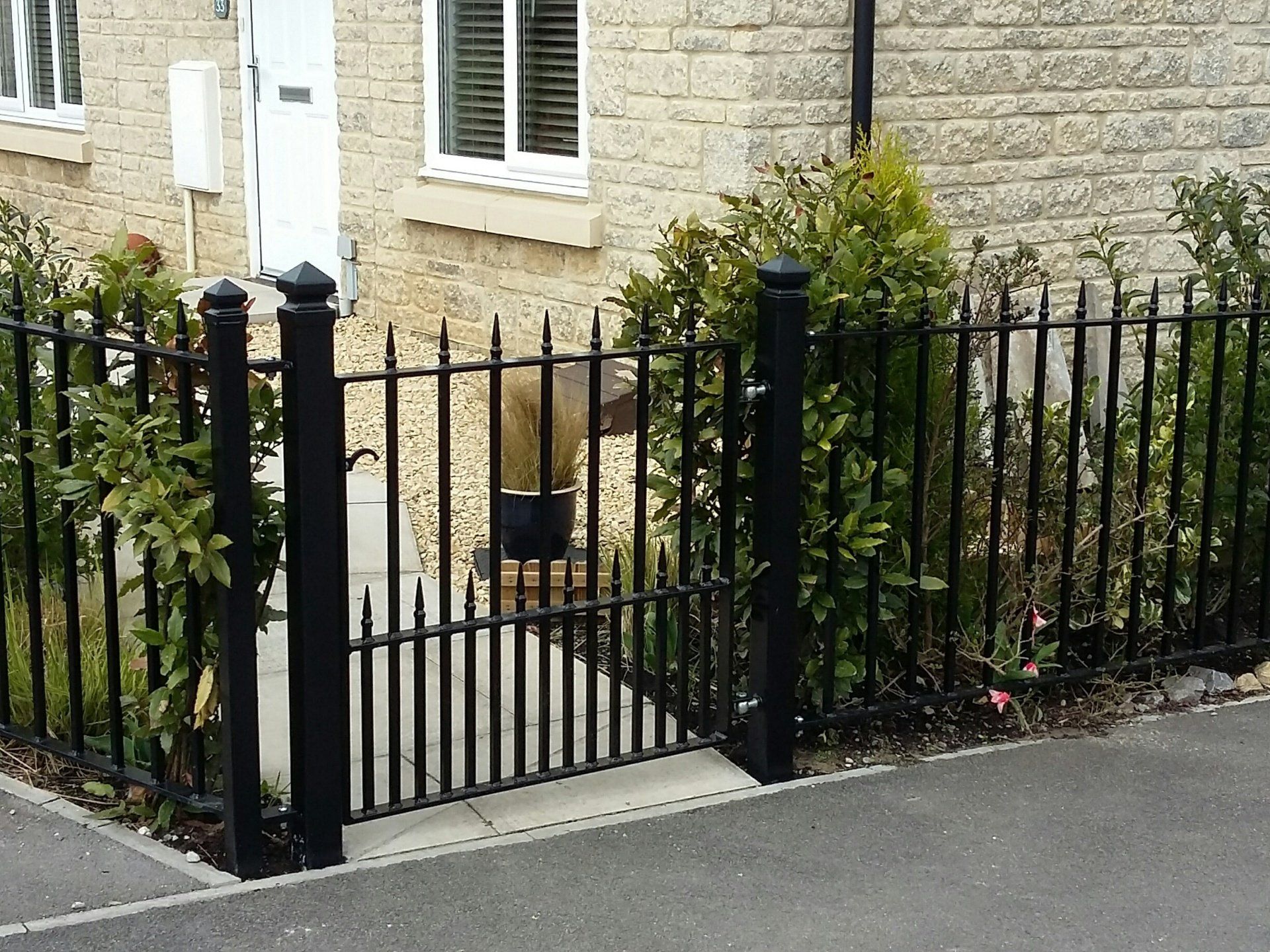 Black metal fence and gate in front of a stone building with green shrubs on either side.