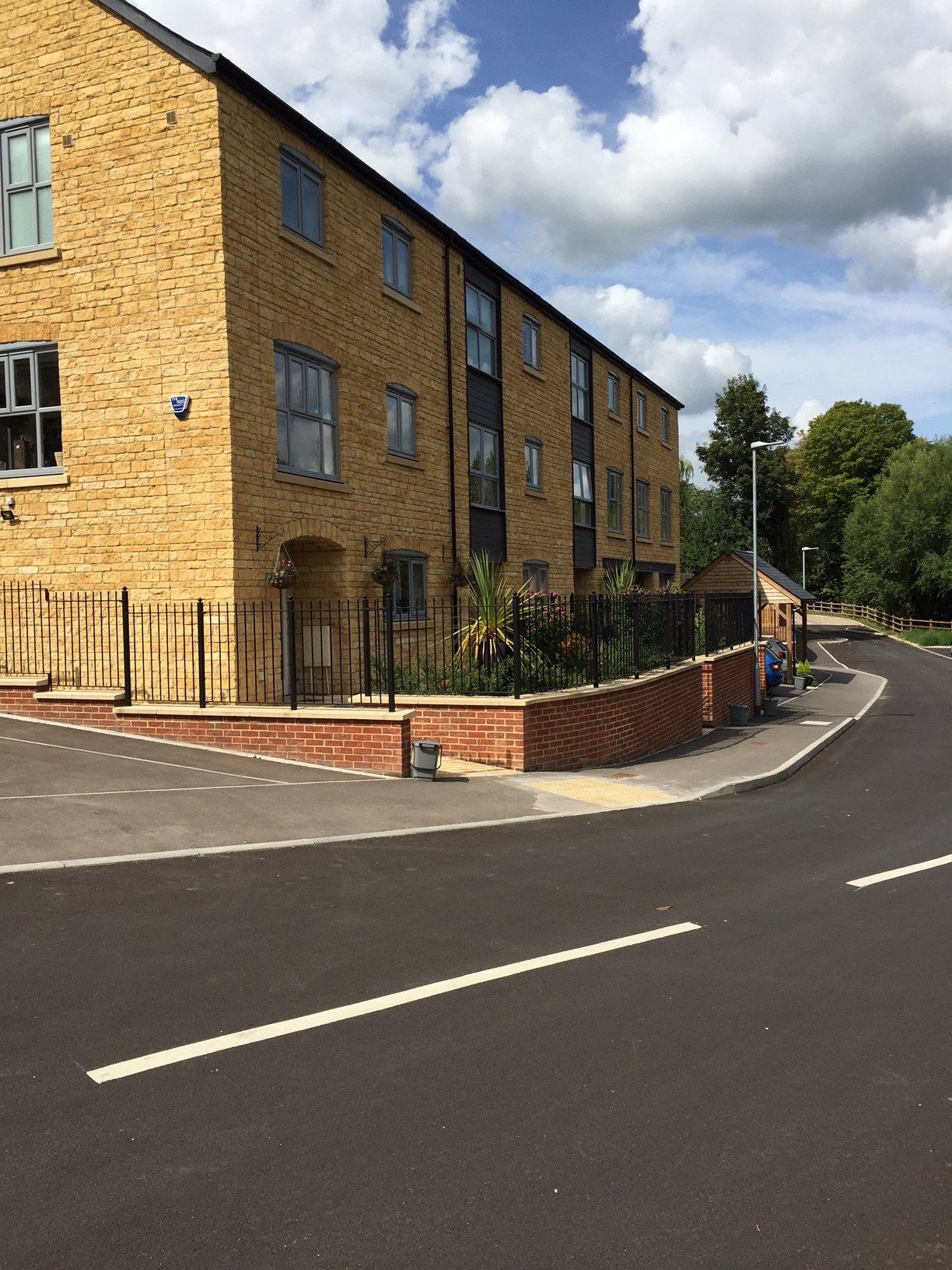 Yellow brick apartment building along a curved street with landscaping and a black fence.