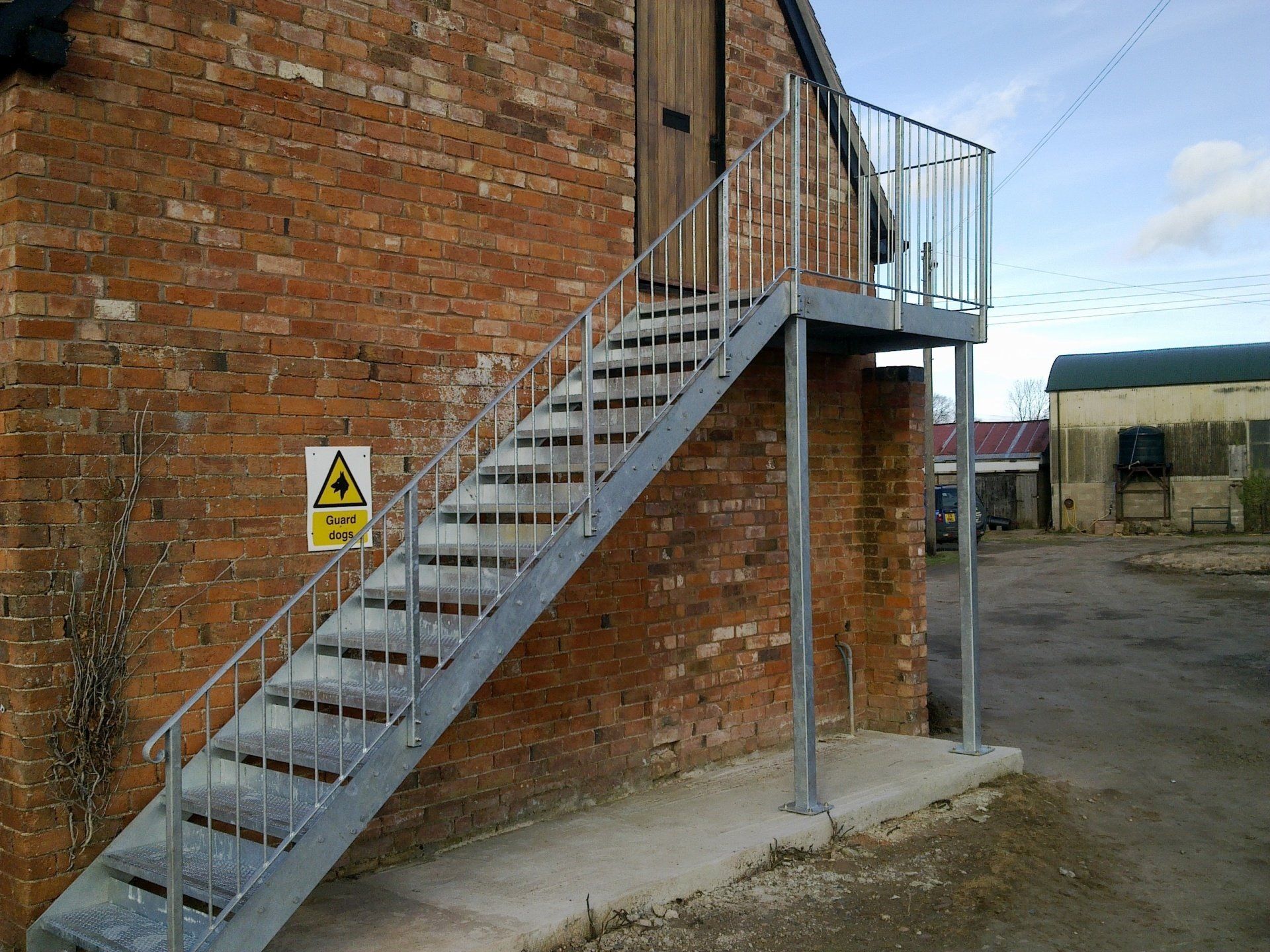 Metal staircase attached to a brick building, leading to a doorway. A hazard sign is visible.