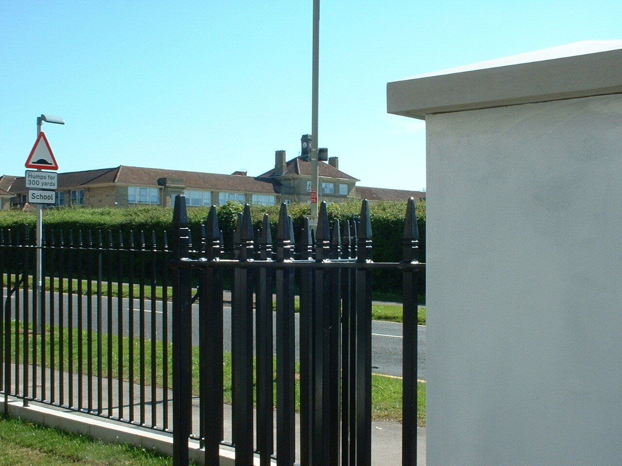 Black spiked fence in front of a building with a tall pole. Blue sky.
