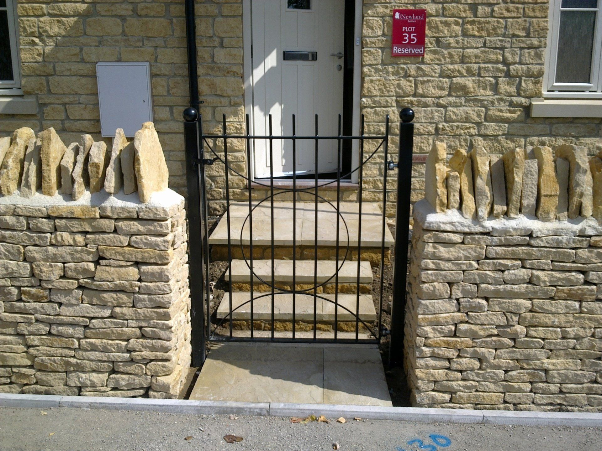 Black gate in front of a stone building with steps leading to a white door.