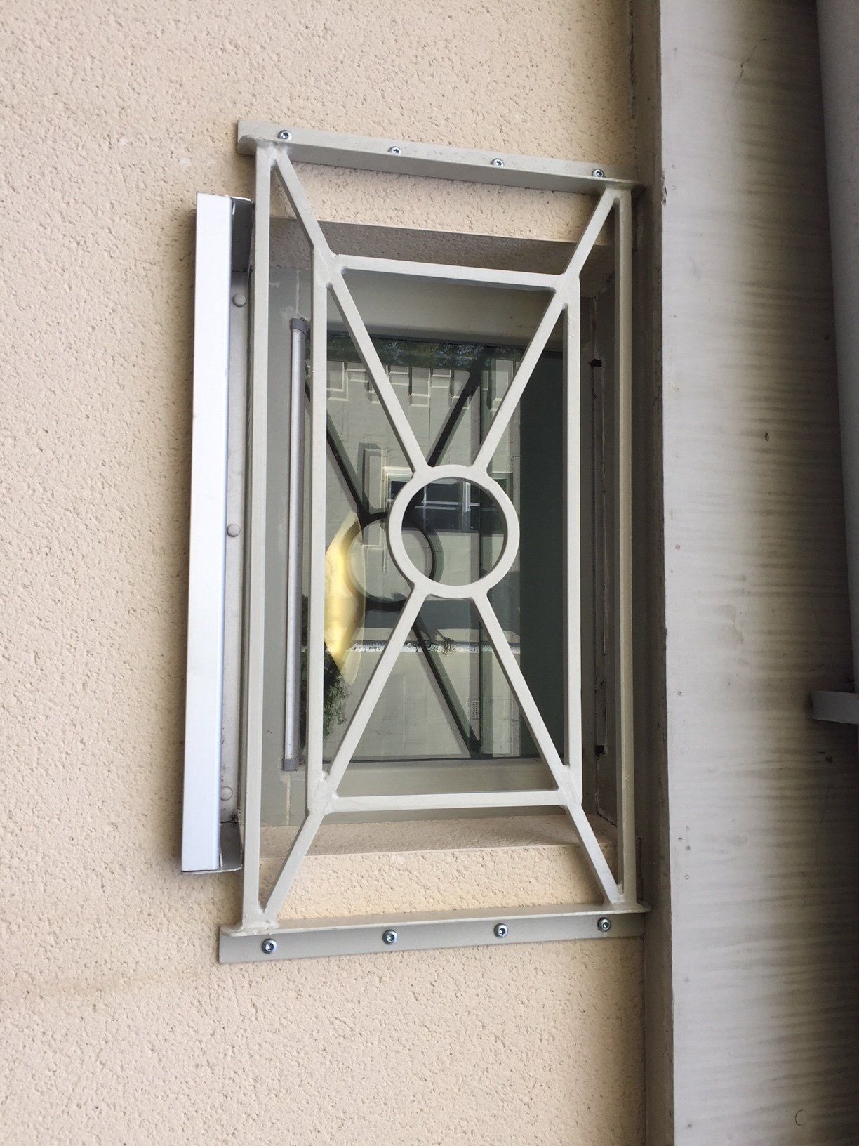 White metal security bars on a window in a beige building exterior.