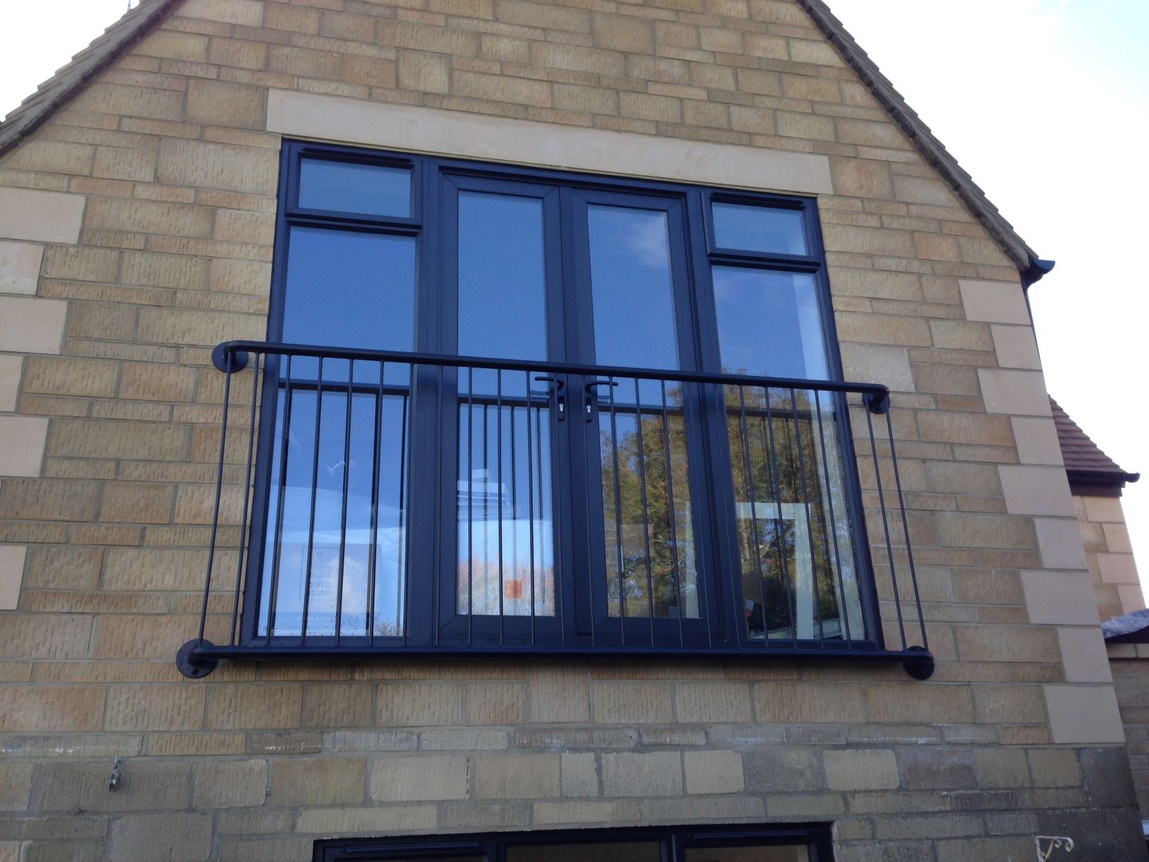 Black framed French doors with balcony on a tan brick building.