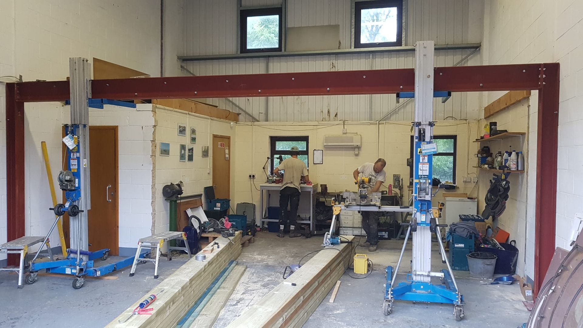 Workshop interior with car lift supports and people working at tables.