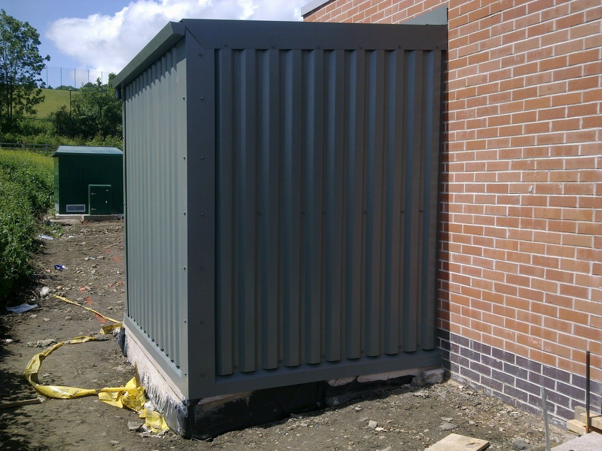 Green corrugated metal equipment enclosure next to a brick building.