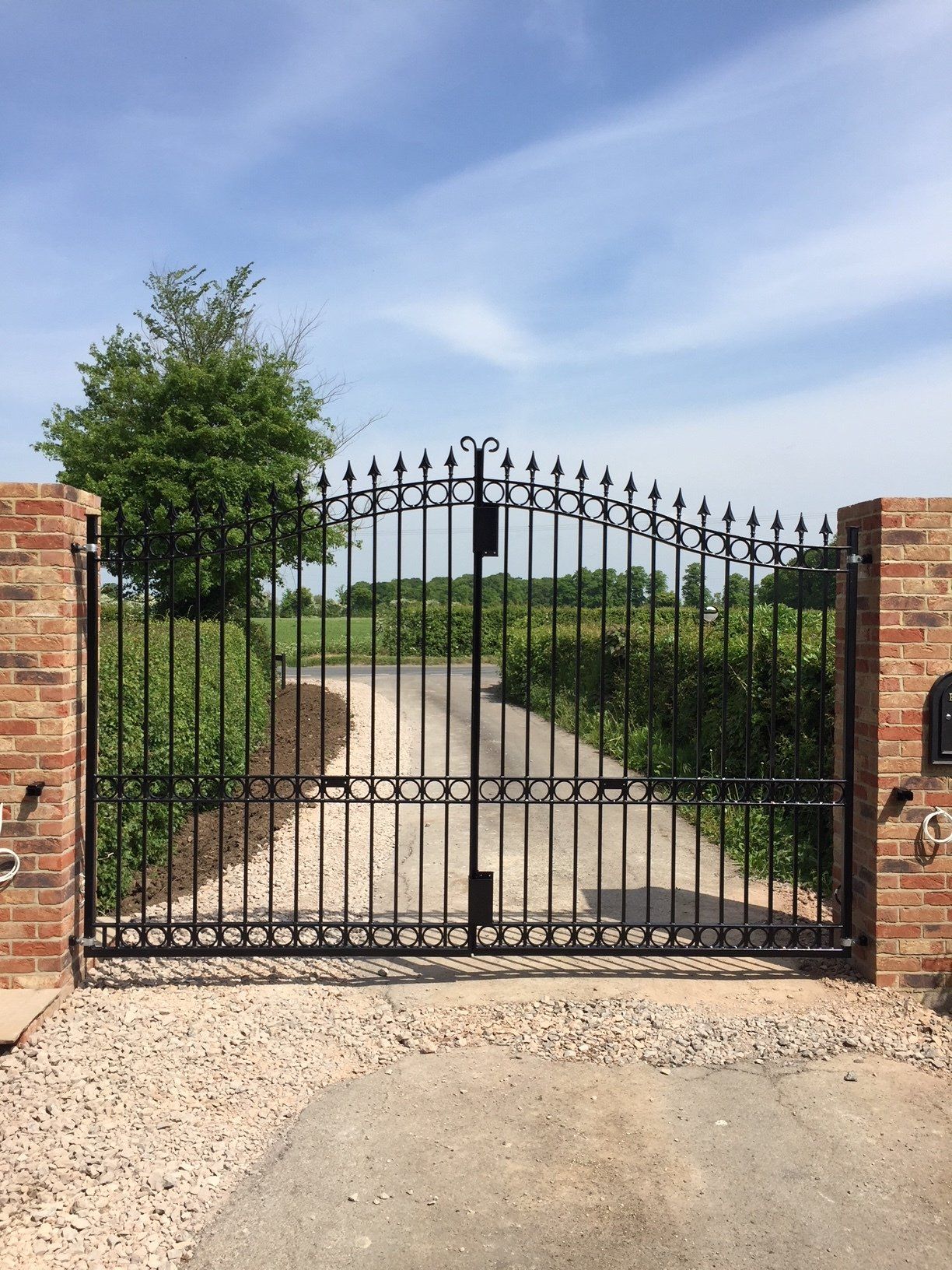 Black metal gates with arched top, between brick pillars, opening to gravel drive.