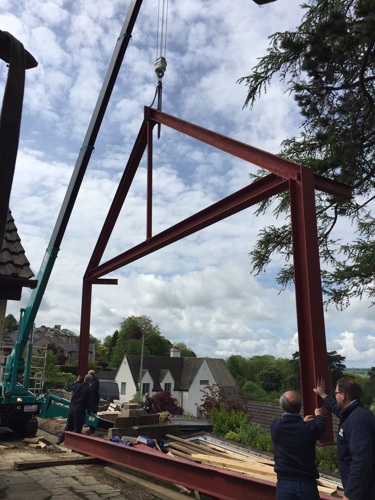 Crane lifting a red steel frame for construction; workers guiding the structure outdoors.