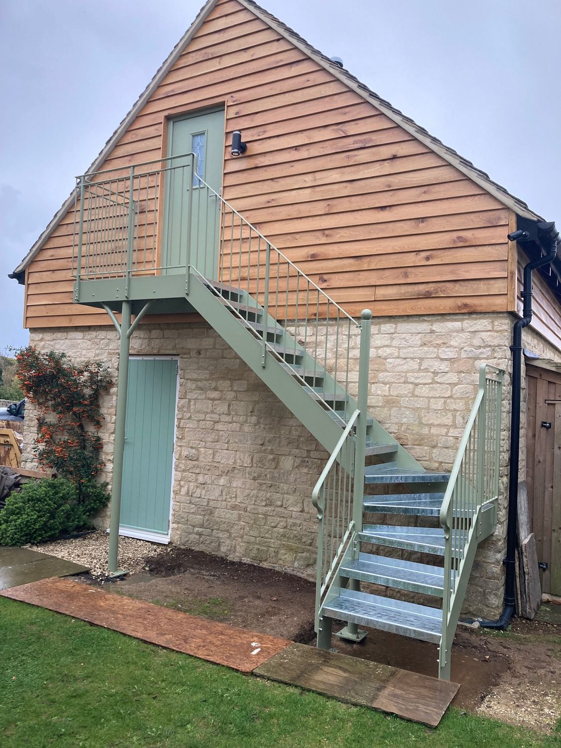 Green metal staircase attached to a two-story building with a wooden upper story and stone lower story.