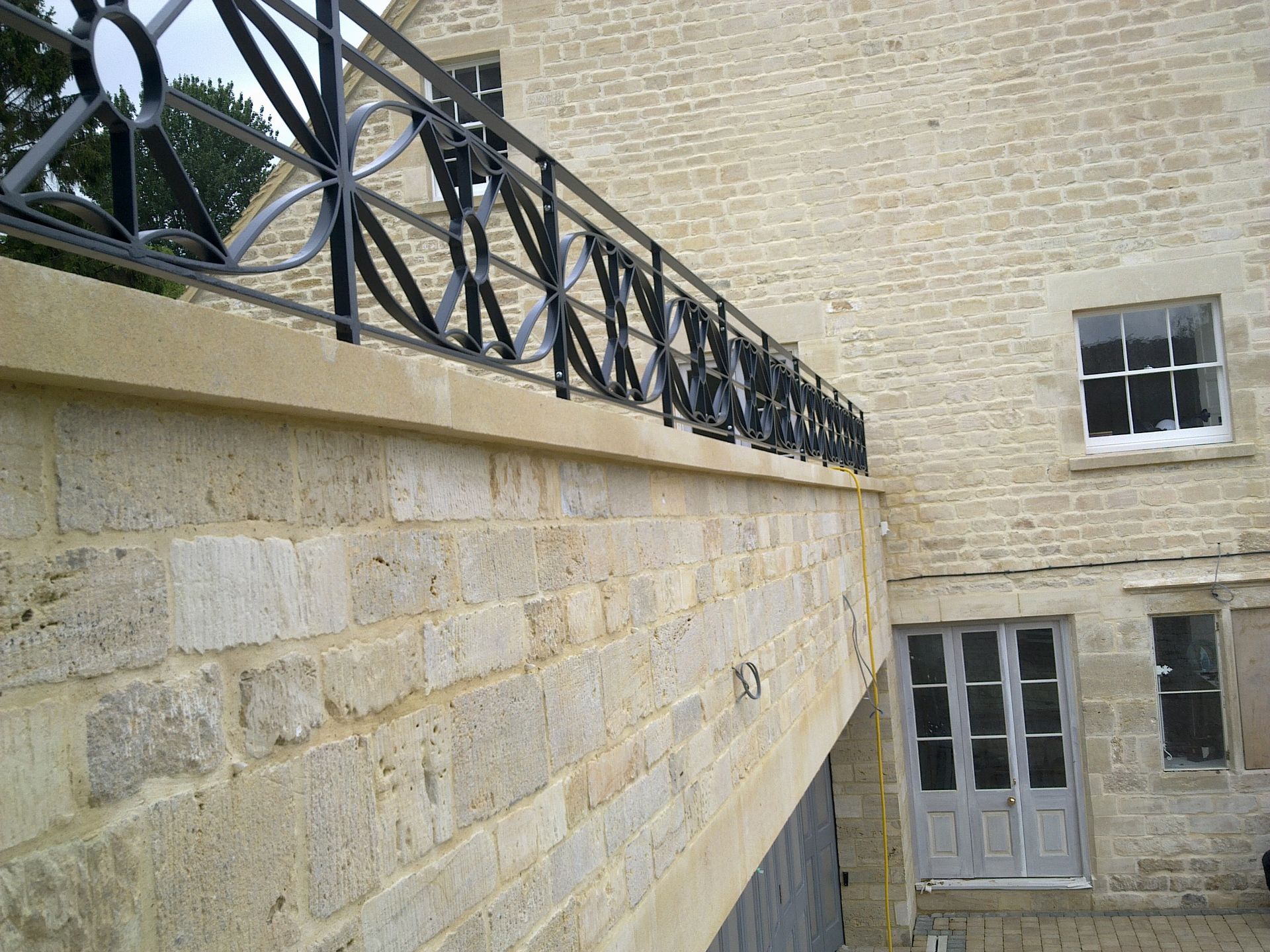 Stone building exterior with black wrought-iron railing, windows, and light gray doors.