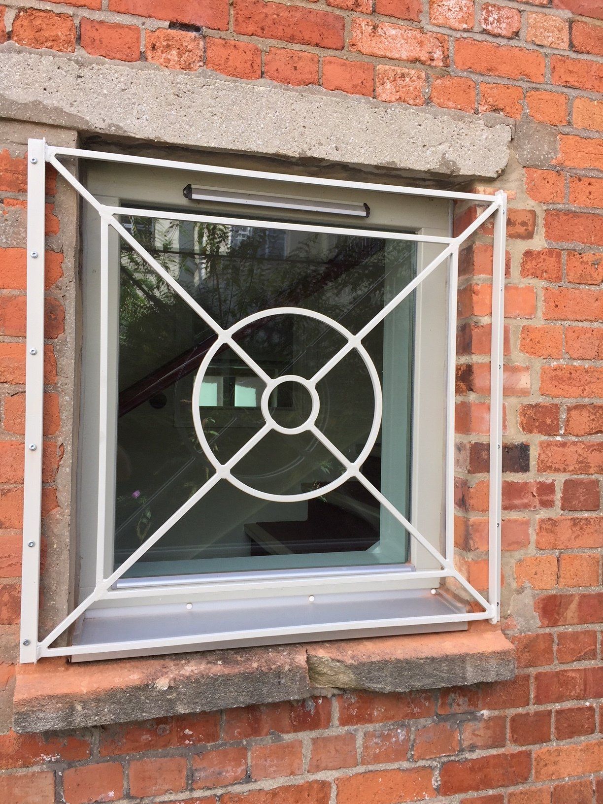 White metal security grille on a basement window set in red brick.