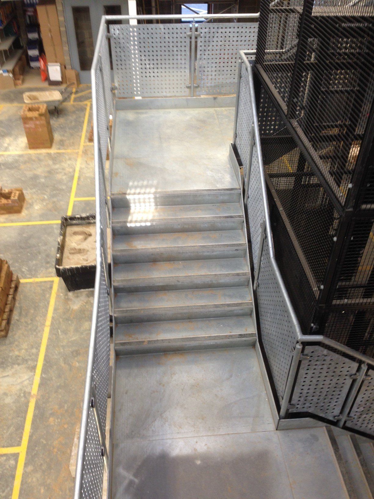 Staircase with metal railings and perforated panels, leading up from a concrete floor in a factory setting.