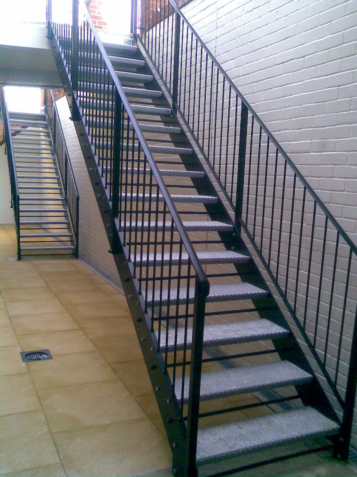 Black metal staircase with carpeted steps against a white brick wall.