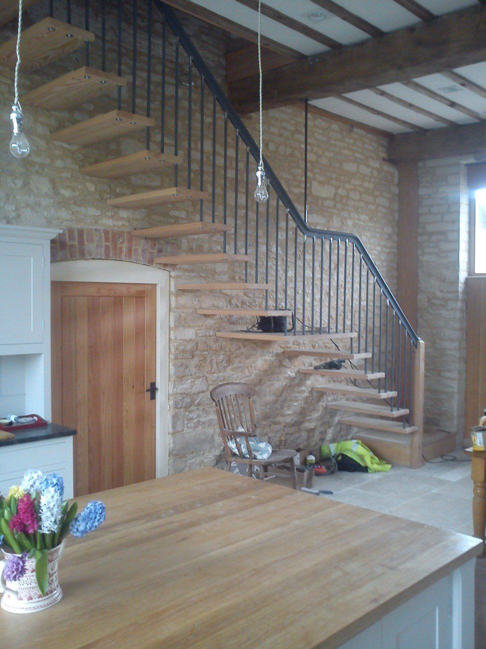 Wooden staircase with black metal railing, against a stone wall in a home.