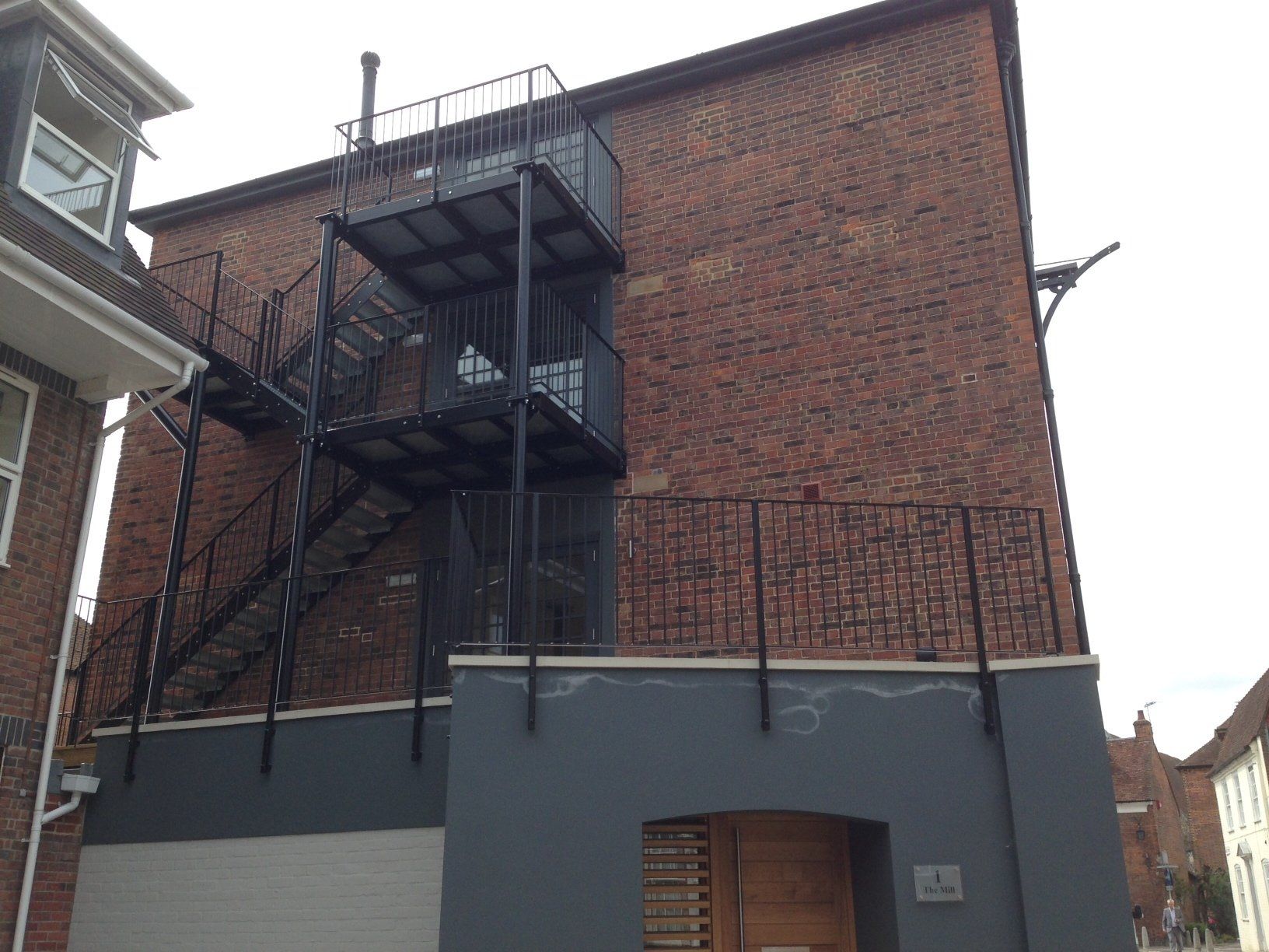 Brick building with black fire escape. Gray painted bottom section with a wooden door.