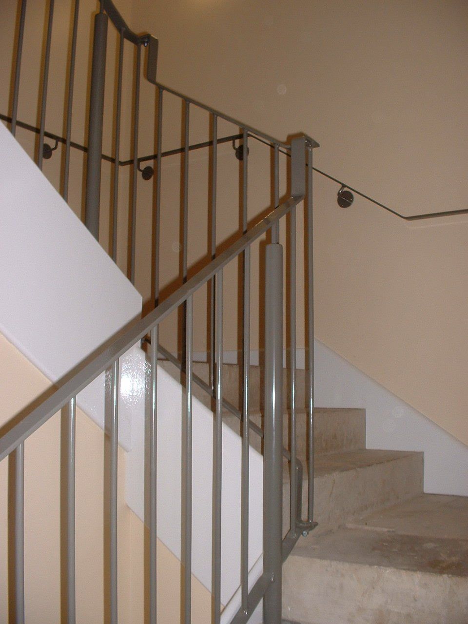 Gray metal staircase railing, tan walls, and concrete stairs.