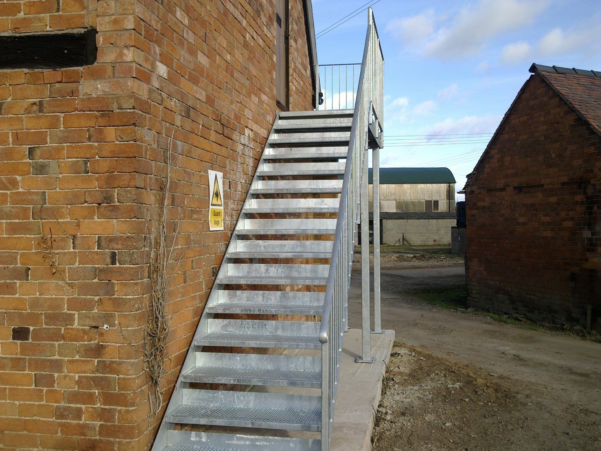 Metal exterior staircase against a brick building; pathway to the right, other buildings in background.