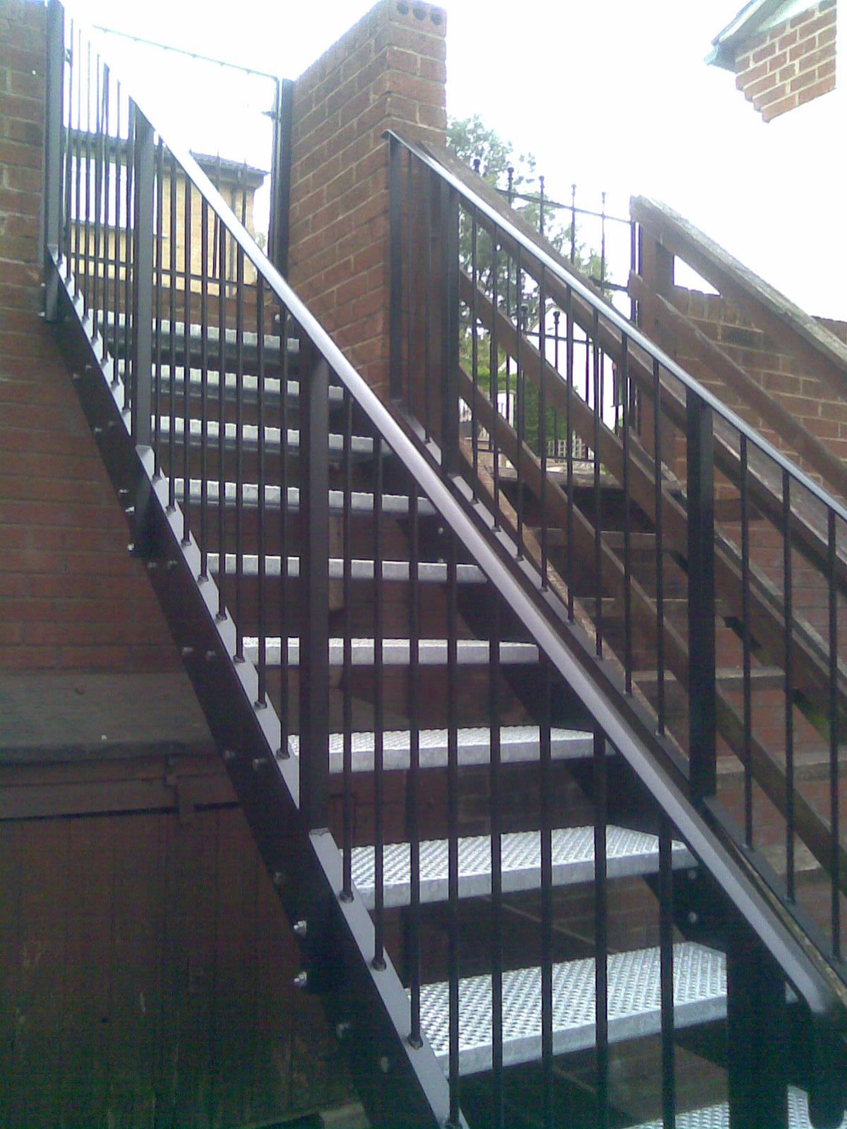 Outdoor metal staircase with black railings and brick walls.