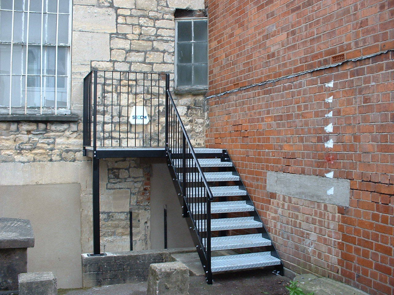 Exterior metal staircase leading down between stone and brick walls.