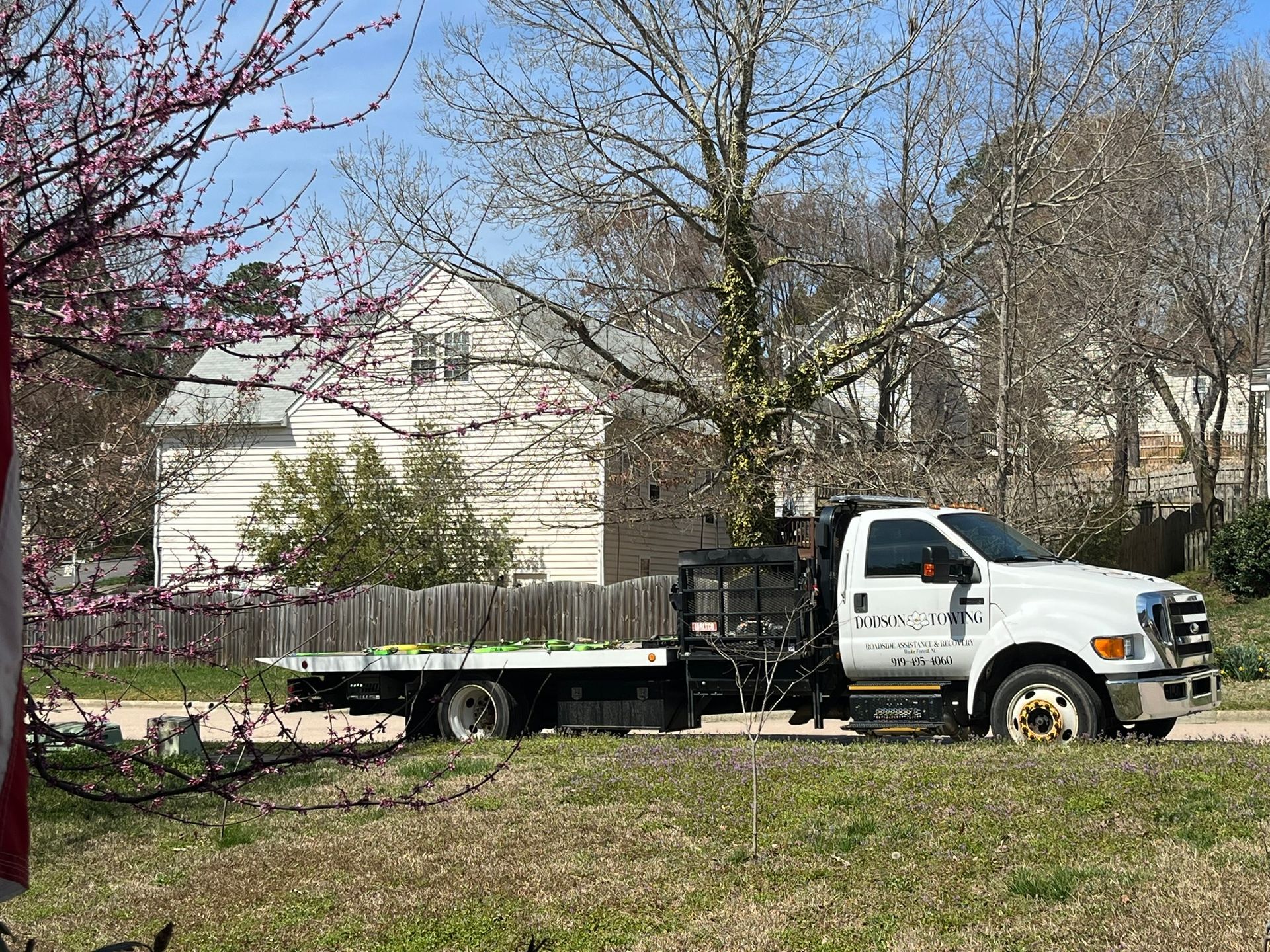 A white tow truck is parked in a grassy field in front of a house.