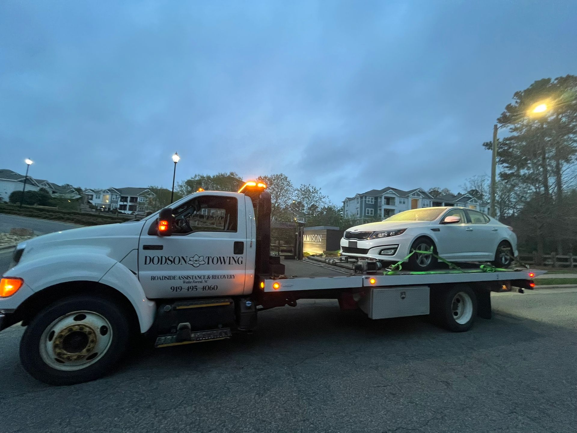 A white tow truck is towing a white car.