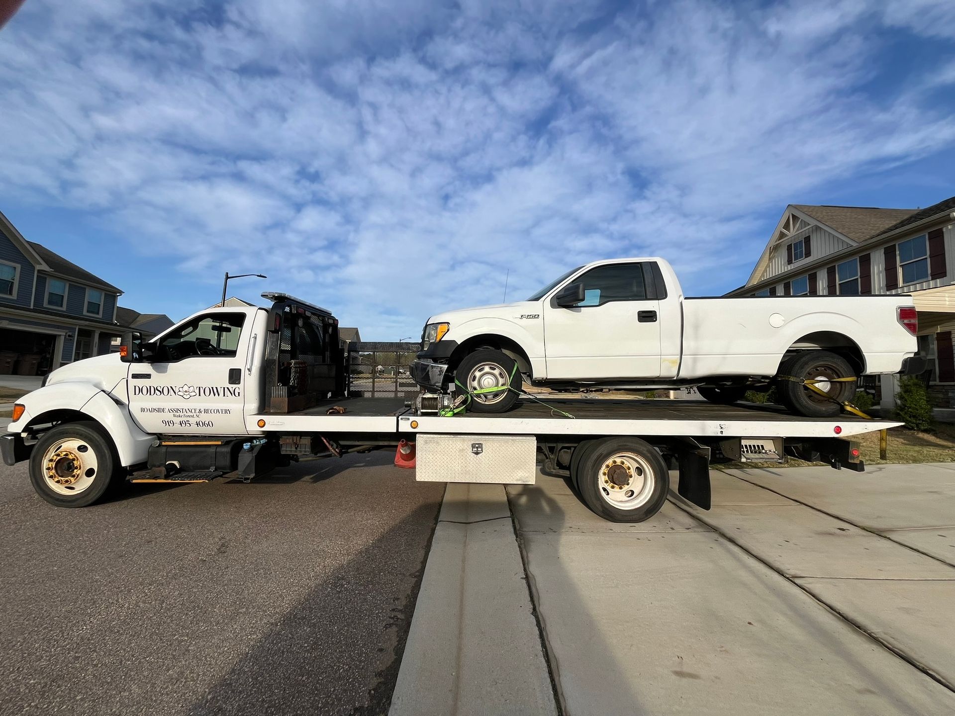 Two white trucks are sitting on top of a tow truck.
