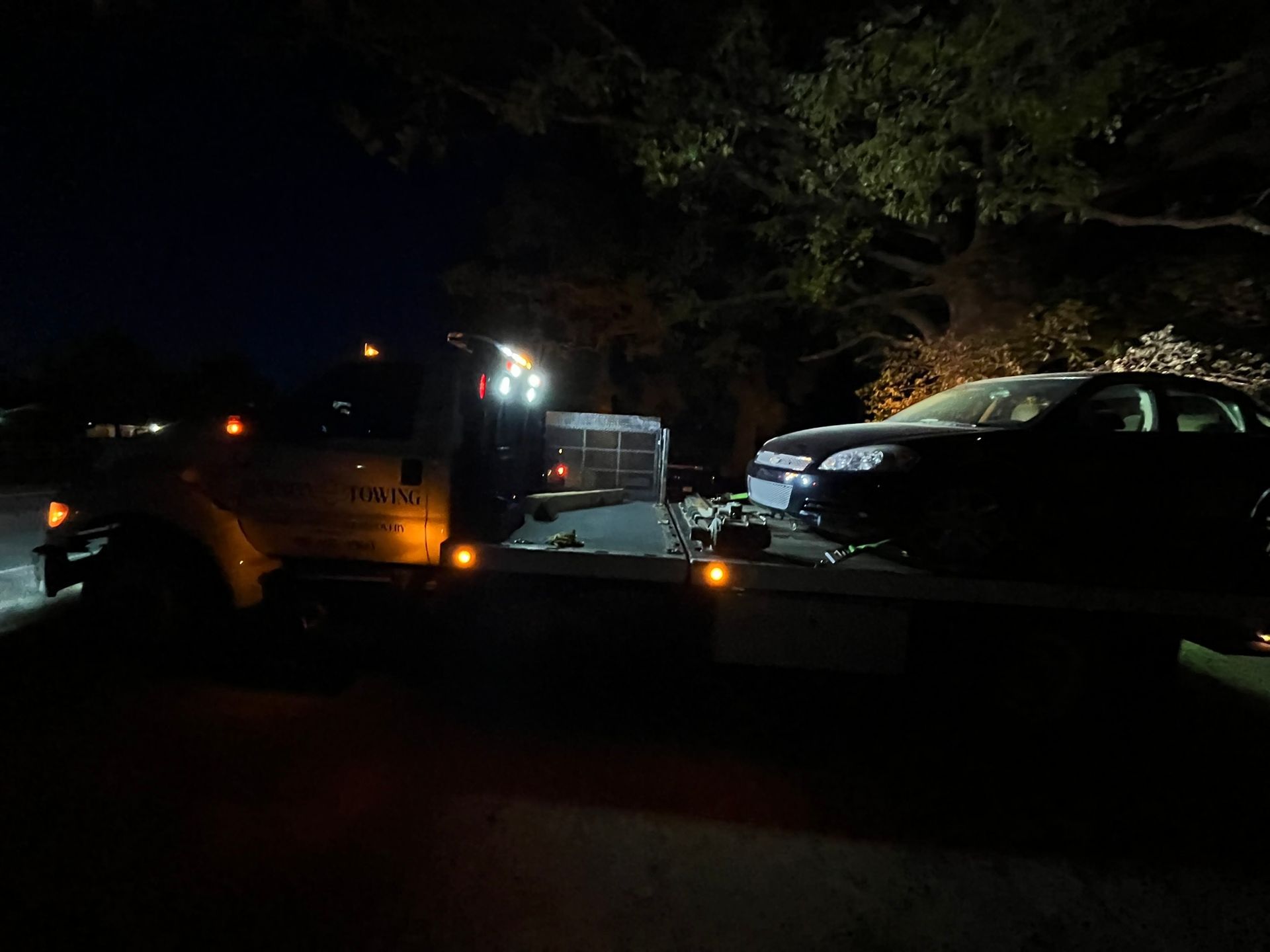 A car is being towed by a tow truck at night.