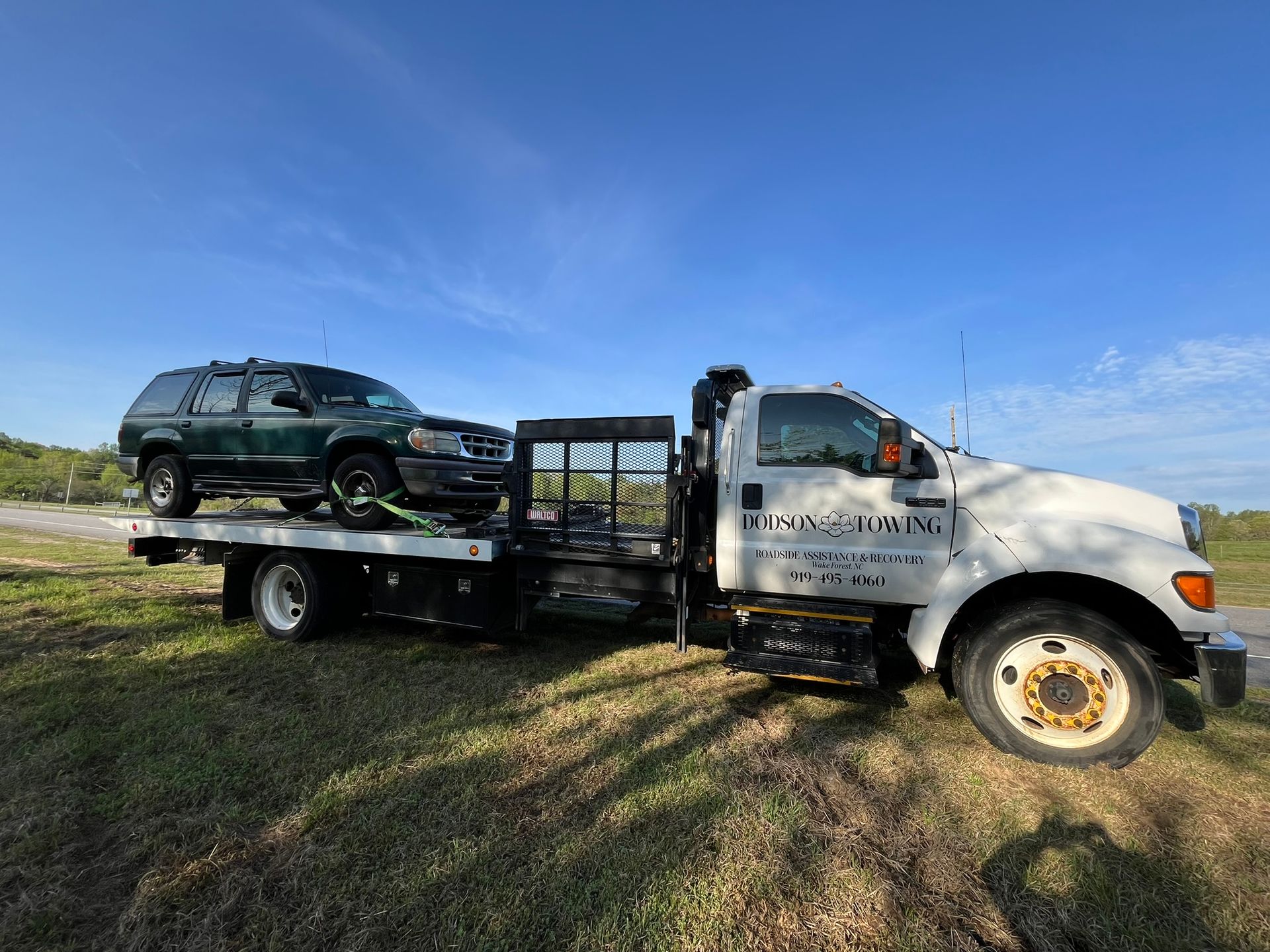 A tow truck with a green suv on the back of it.