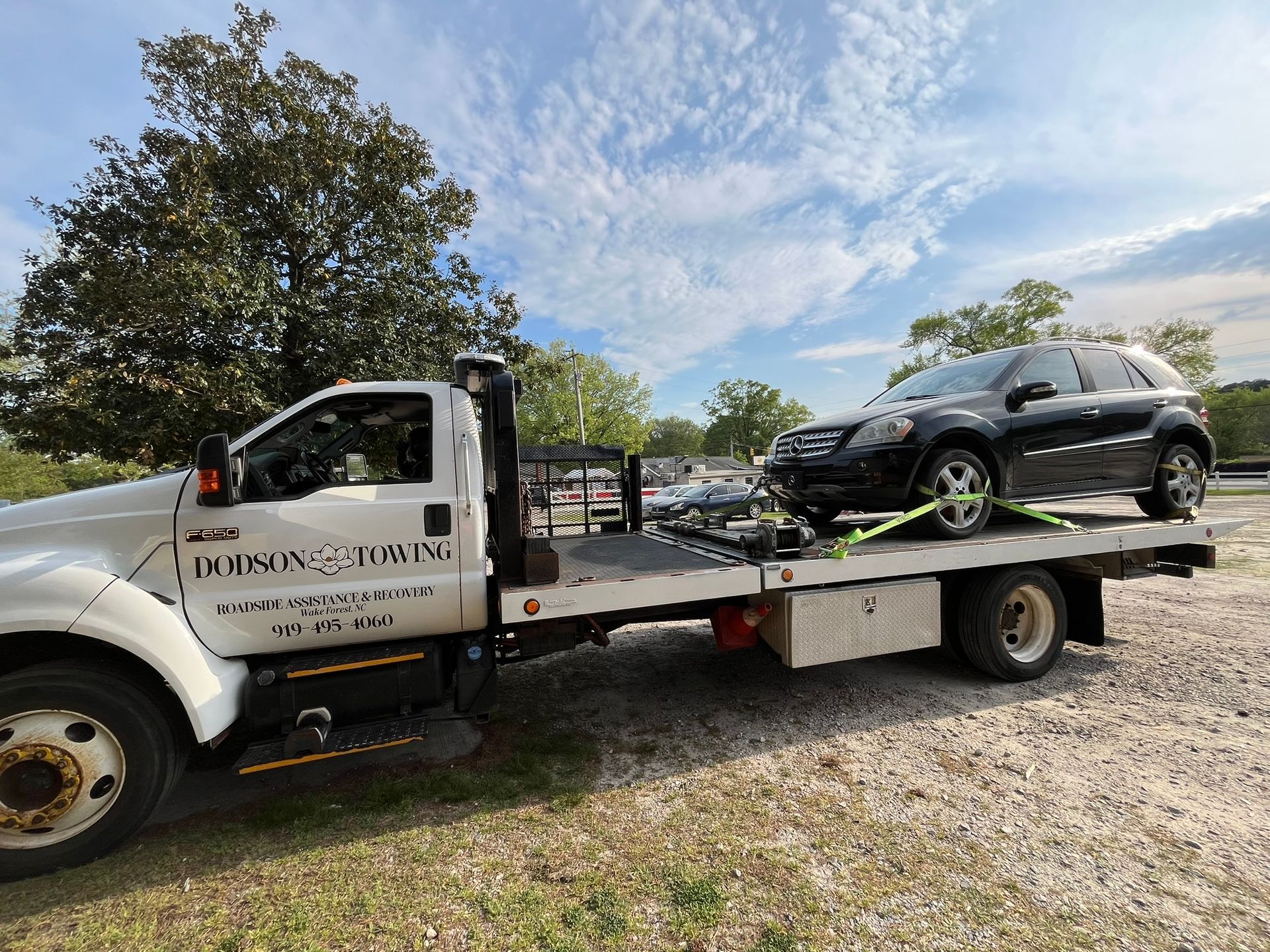 A tow truck is carrying a black suv on the back of it.