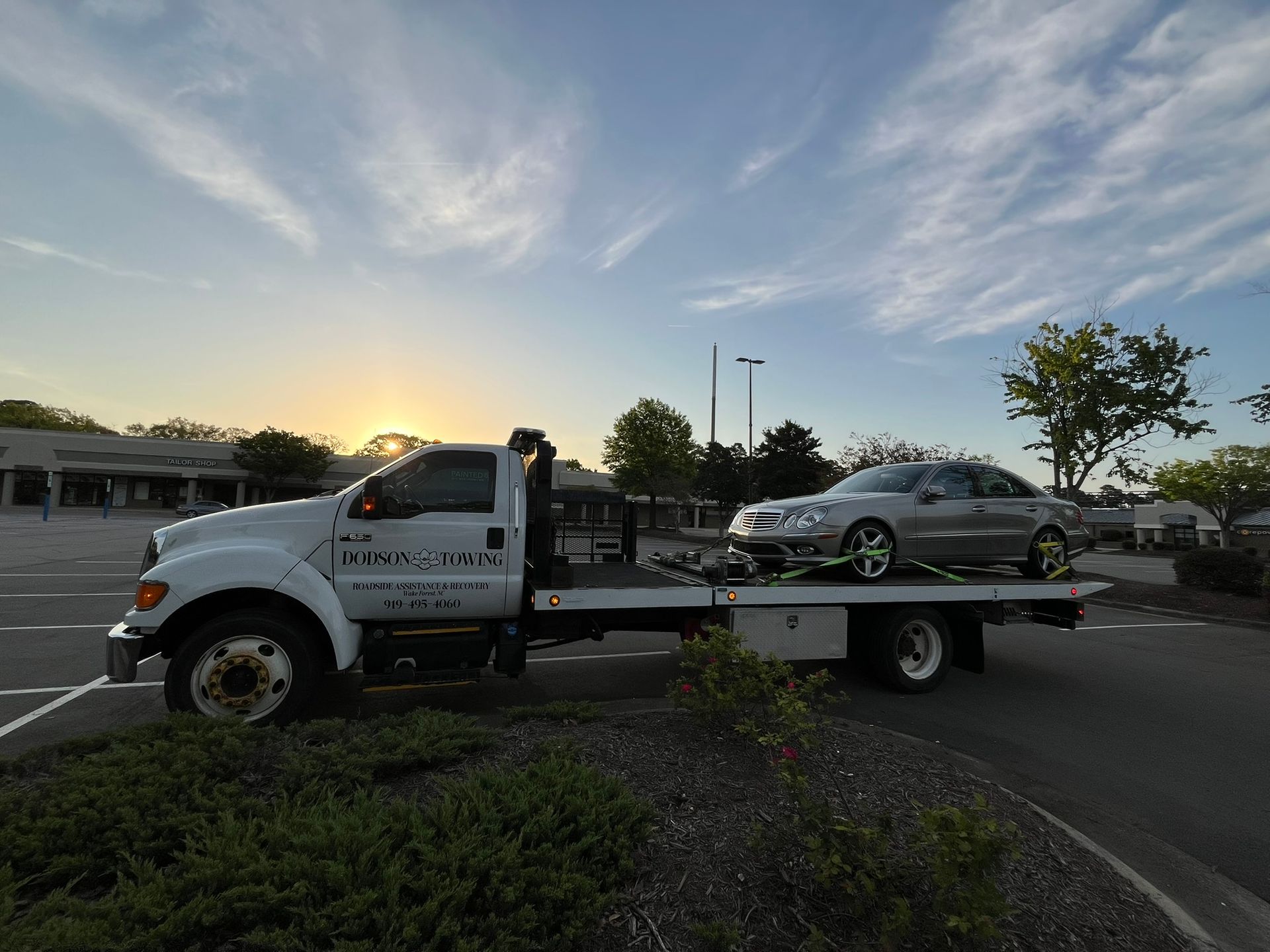 A tow truck with two cars on the back is parked in a parking lot.