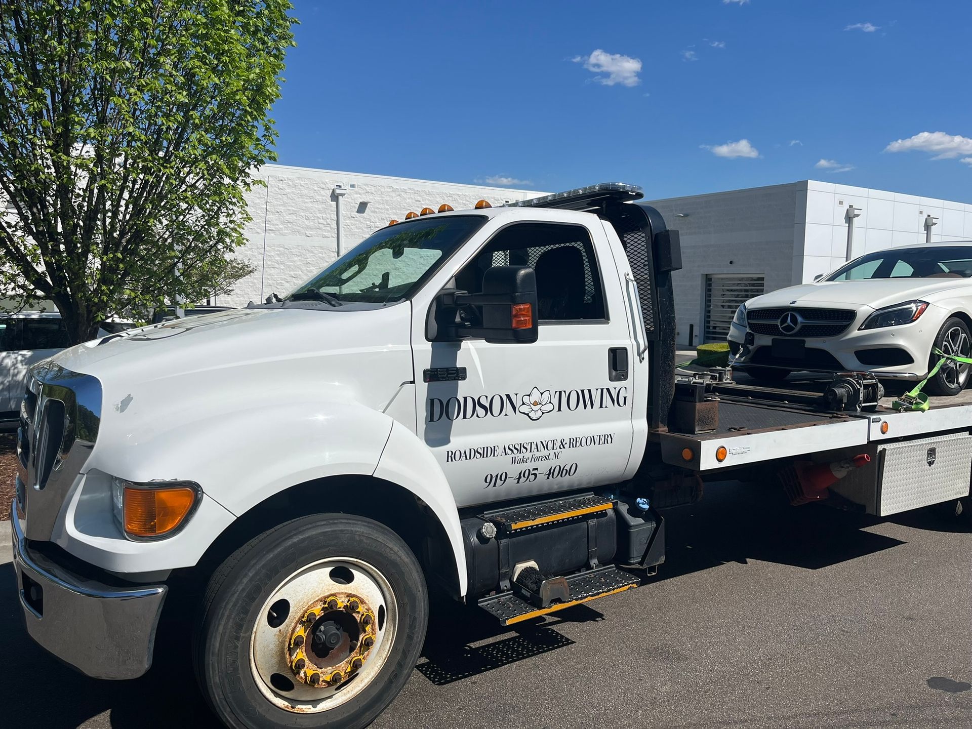 A white tow truck with a white car on the back is parked in front of a building.