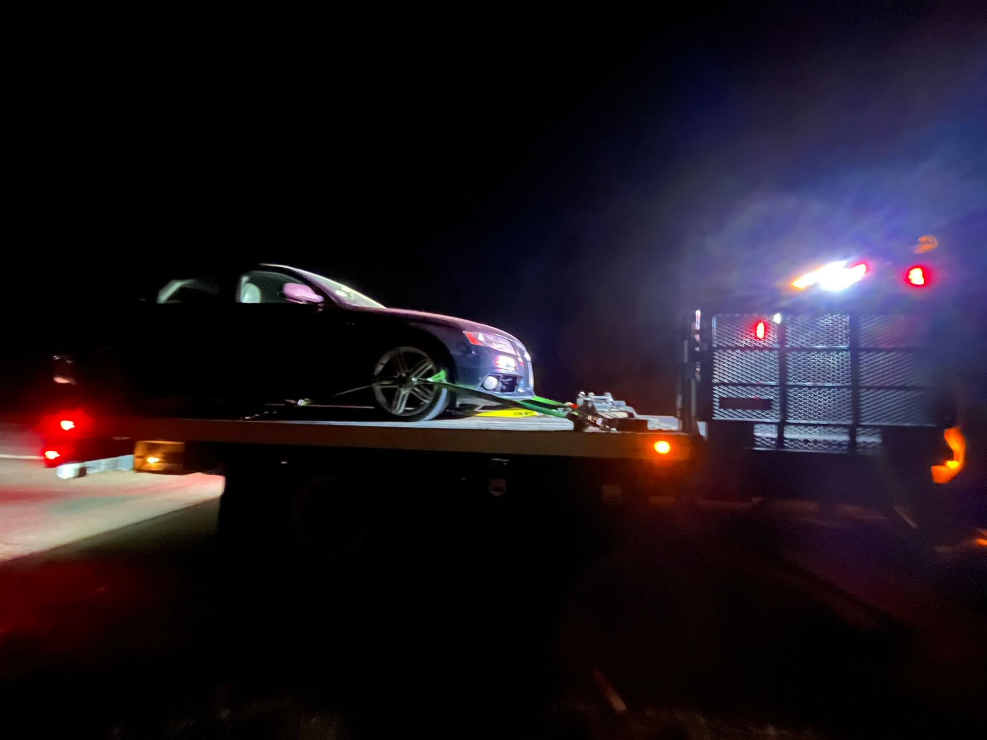 A car is being towed by a tow truck at night.