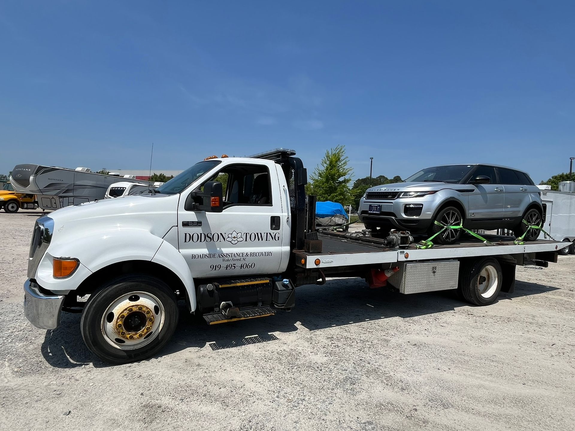 A tow truck is carrying a silver range rover on the back of it.