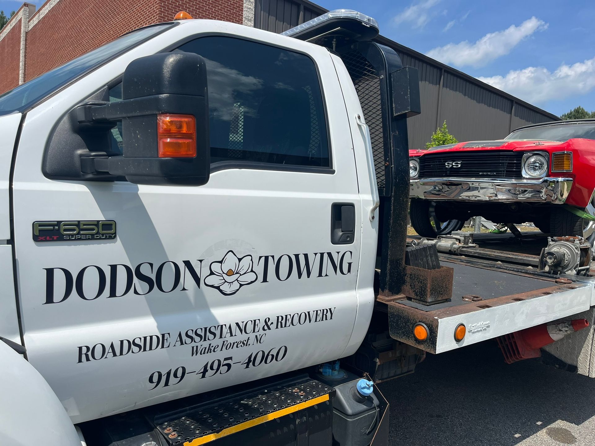 A white tow truck with a red car on the back of it.