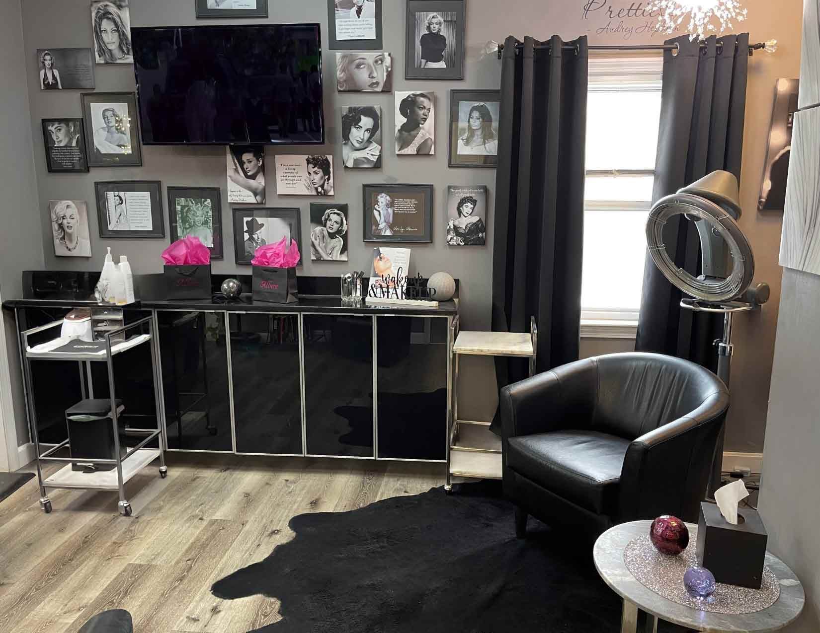 A modern beauty salon studio featuring black furniture, a gallery wall of framed portraits, and a black armchair.