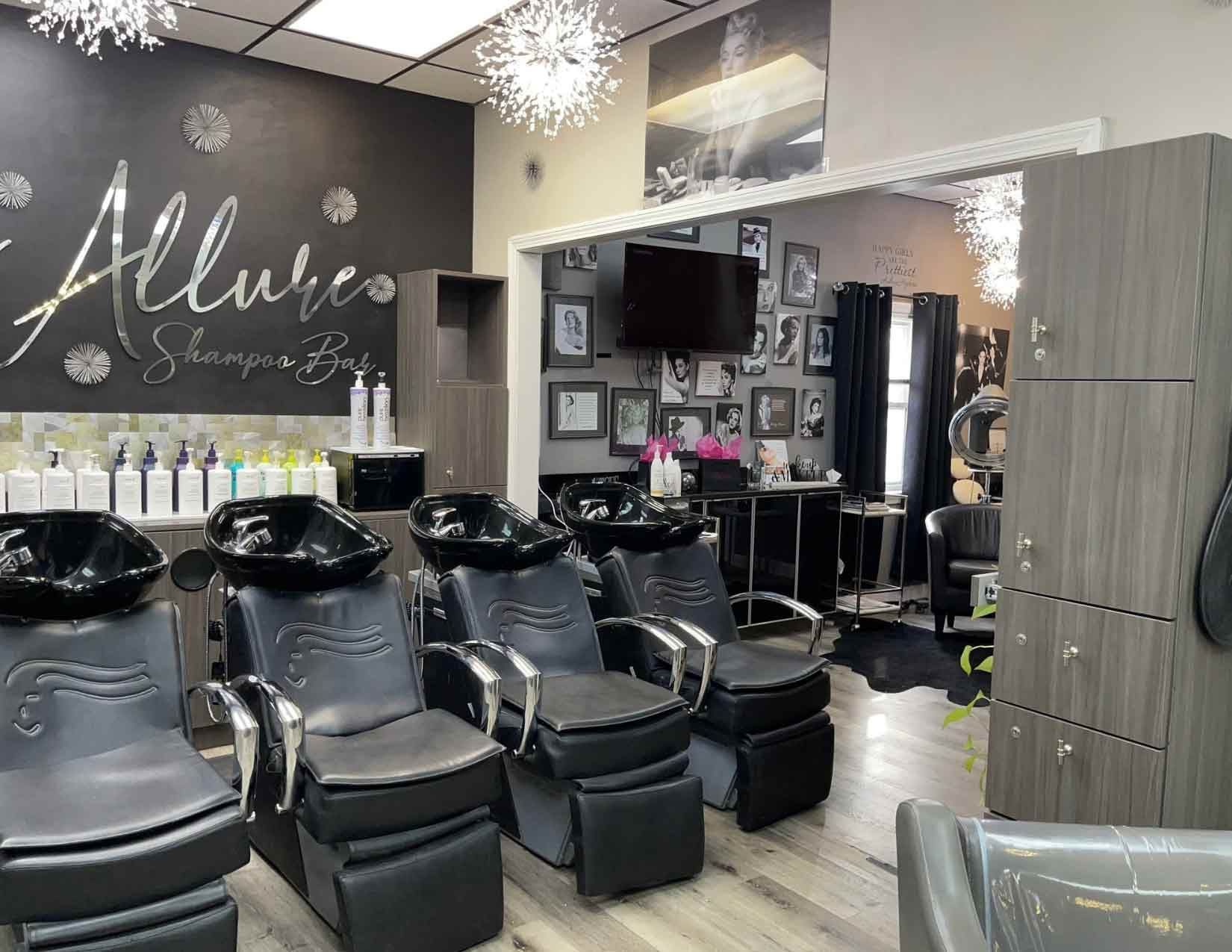 Modern hair salon interior with three black shampoo chairs in a row, light wood floors, and a branded accent wall.