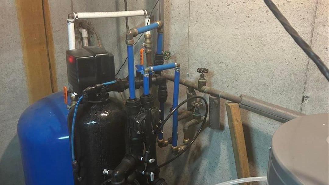 A water filter is sitting in a basement next to a water tank.