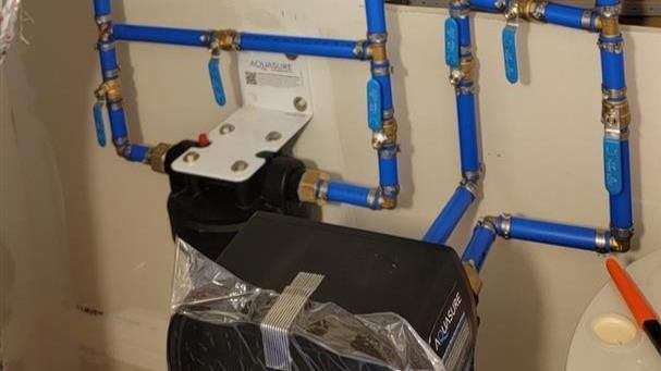 A water filter is attached to a wall with blue pipes.