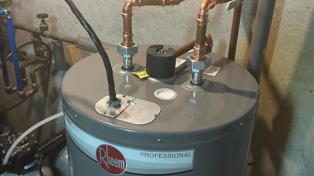 A rheem water heater is sitting in a basement next to copper pipes.