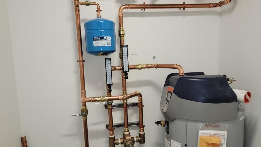 A room with a water heater and copper pipes.