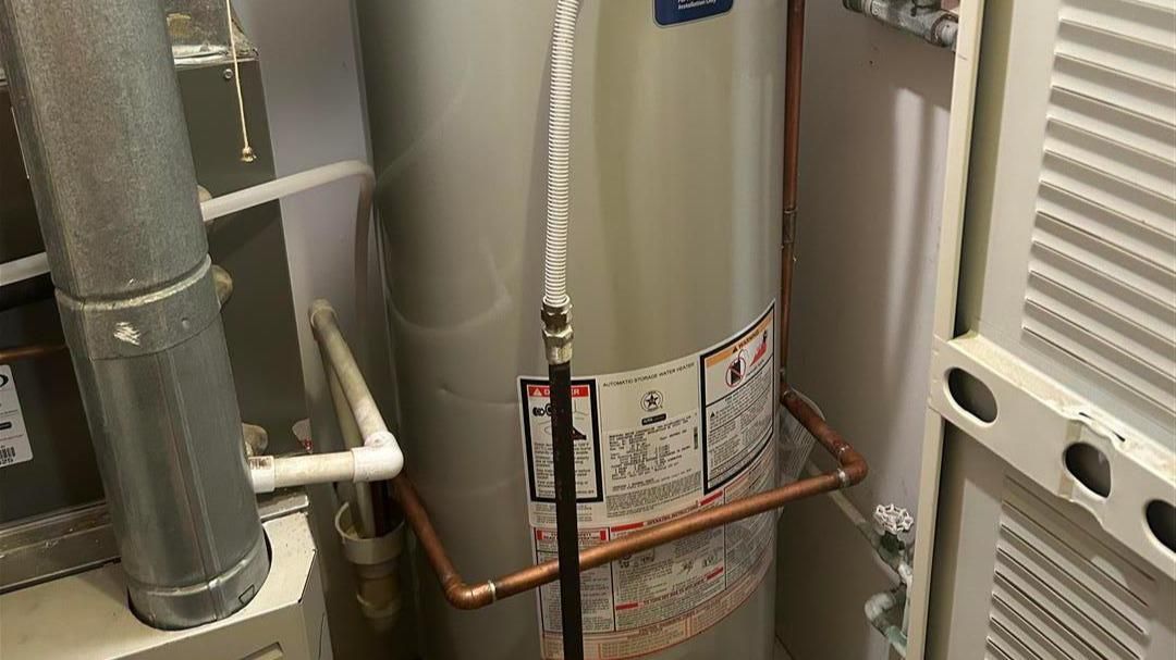A water heater is sitting in a room next to a furnace.