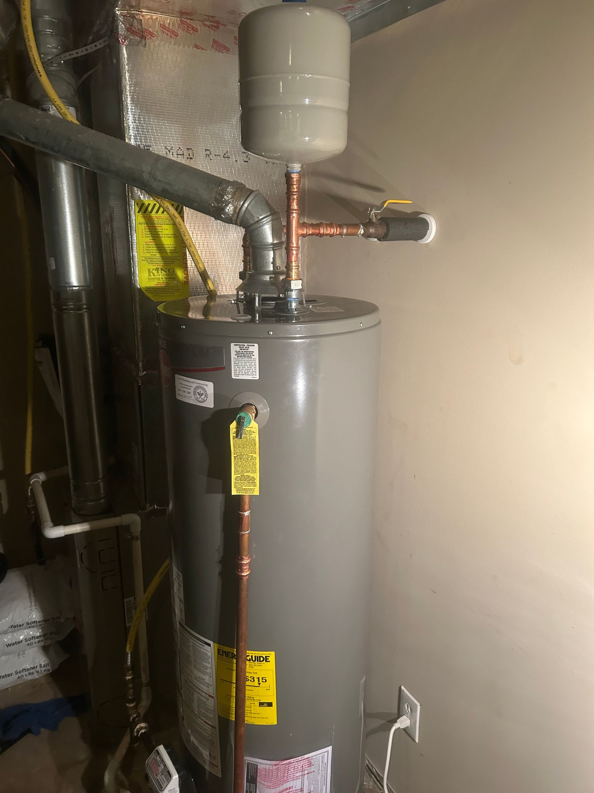 A water heater is sitting in a basement next to a wall.