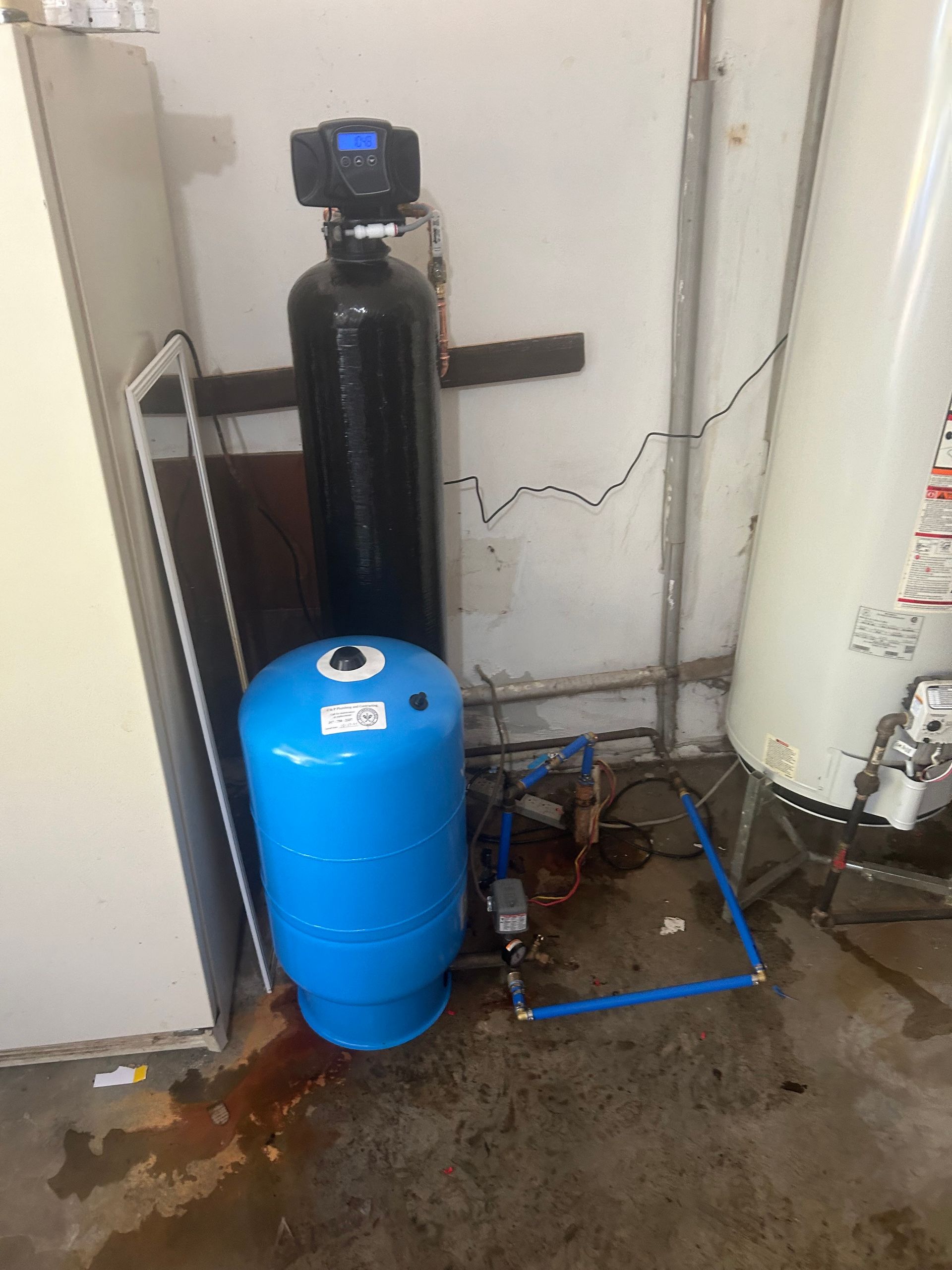 A water filter is sitting next to a water heater in a garage.