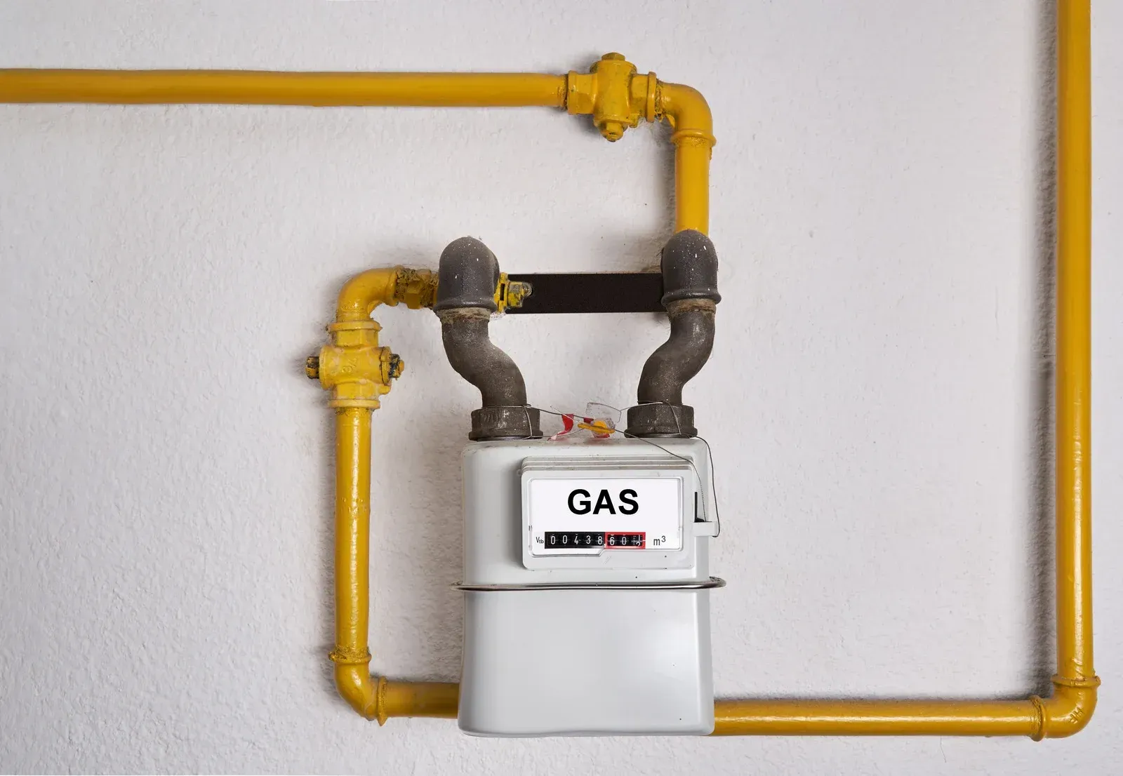 A gas meter is attached to a yellow pipe on a wall.