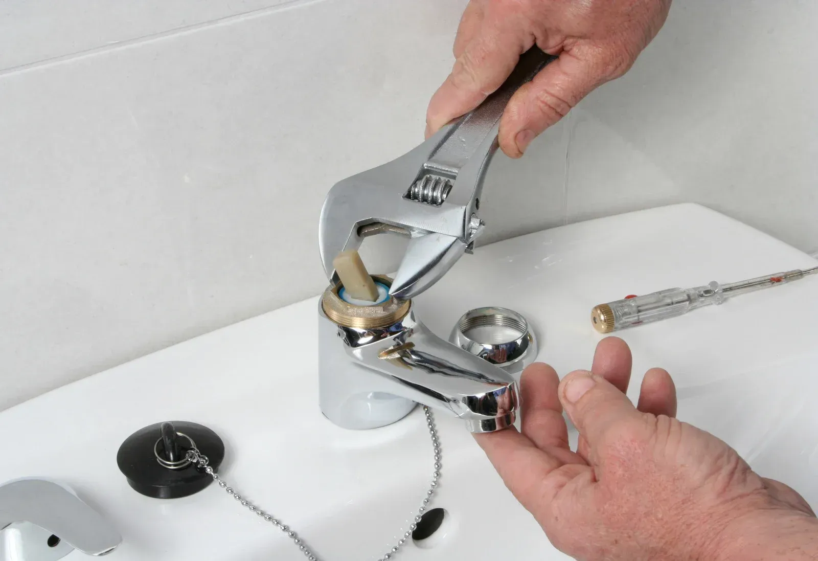 A person is fixing a faucet with a wrench.